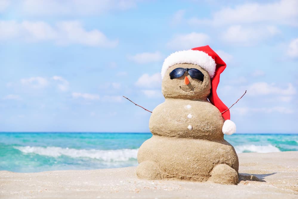 Smiling sandy snowman in red santa hat on the sea beach. Holiday concept can be used for New Year and Christmas Cards